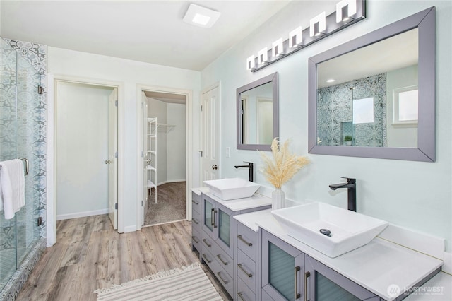 full bath with a spacious closet, a sink, a shower stall, and wood finished floors