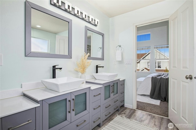 ensuite bathroom featuring double vanity, wood finished floors, a sink, and connected bathroom