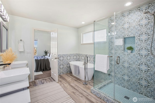 full bathroom featuring a stall shower, wood finished floors, a sink, a freestanding bath, and tile walls