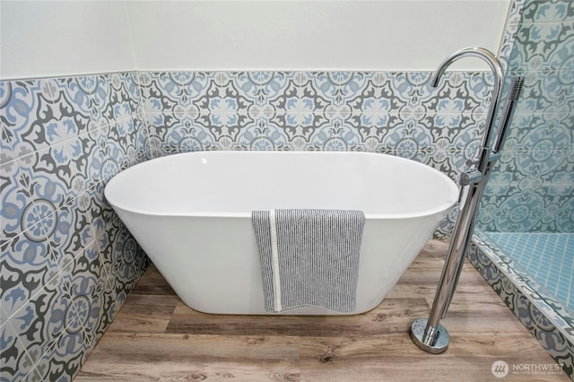 bathroom featuring a freestanding tub, wainscoting, tile walls, and wood finished floors