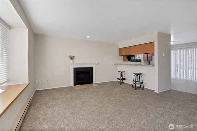 unfurnished living room featuring carpet, a baseboard heating unit, baseboards, and a fireplace with flush hearth