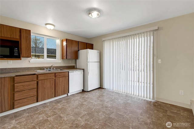 kitchen featuring white appliances, baseboards, brown cabinets, and a sink