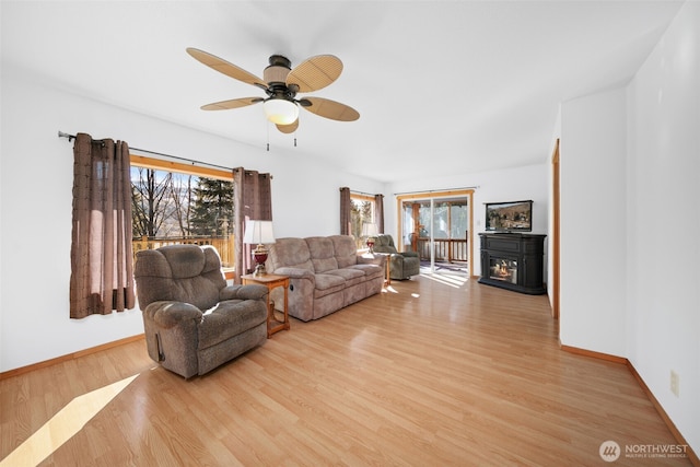 living area featuring light wood-style flooring, baseboards, a ceiling fan, and a glass covered fireplace