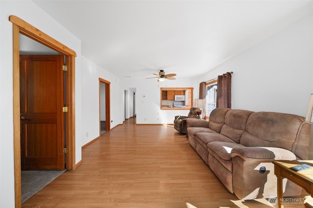 living area with a ceiling fan, light wood-type flooring, and baseboards