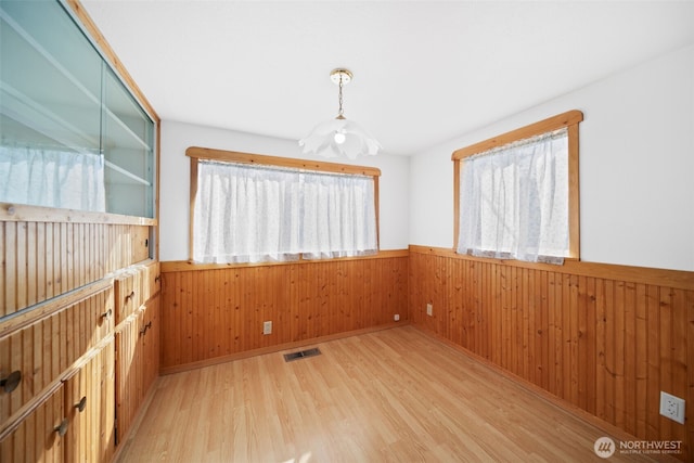 spare room with visible vents, a wainscoted wall, wooden walls, and light wood finished floors