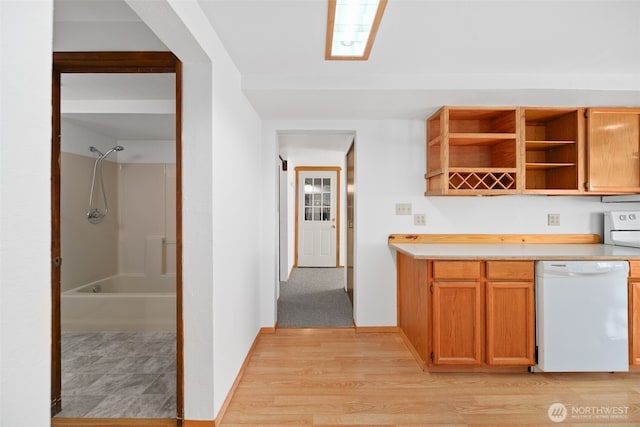 kitchen featuring open shelves, light wood finished floors, white dishwasher, and light countertops