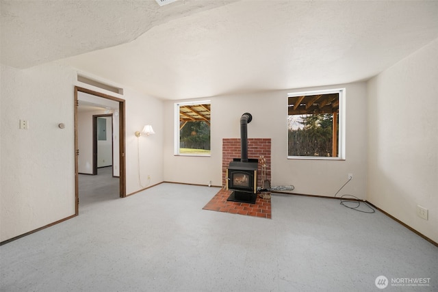 unfurnished living room with a wood stove, a textured ceiling, and baseboards