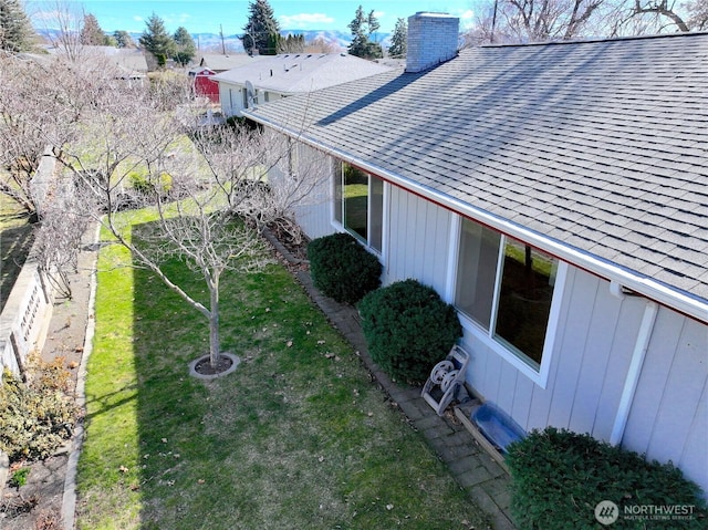 exterior space featuring a chimney, a shingled roof, and a yard