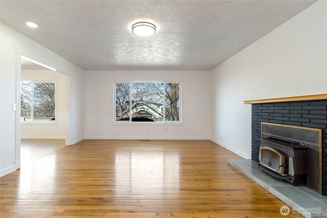 unfurnished living room featuring baseboards, a textured ceiling, a fireplace, and light wood finished floors