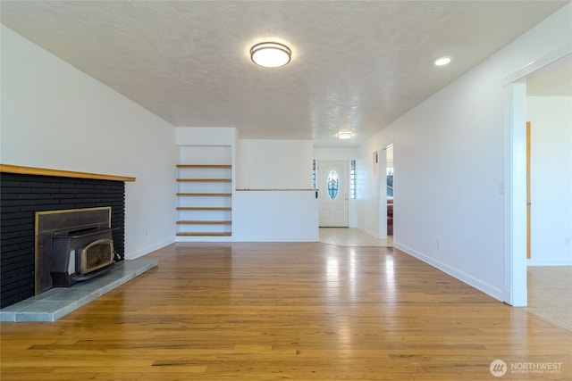 unfurnished living room featuring light wood-type flooring, baseboards, a textured ceiling, and a wood stove