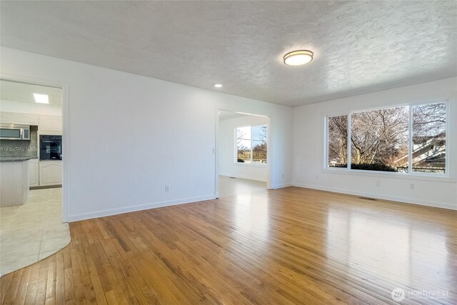 empty room featuring light wood-type flooring, baseboards, a textured ceiling, and visible vents