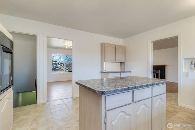 kitchen with dark countertops, black oven, a center island, baseboards, and a fireplace