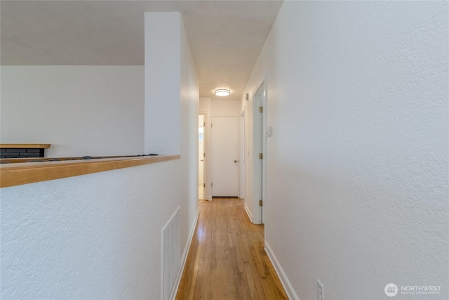 corridor featuring visible vents, baseboards, and light wood-style floors