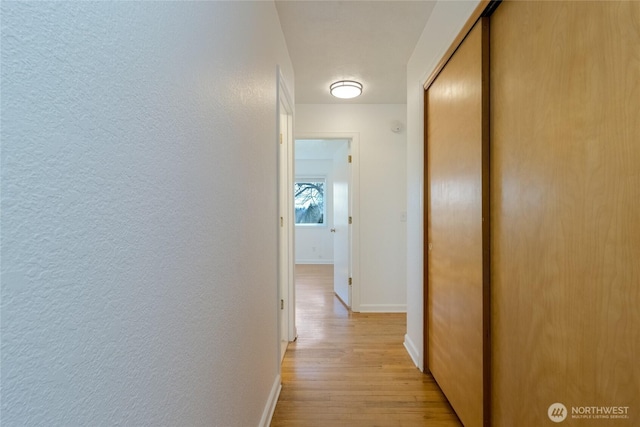 corridor with a textured wall, light wood-type flooring, and baseboards