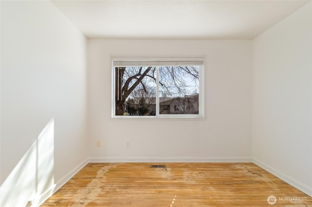 empty room with visible vents, light wood-type flooring, and baseboards