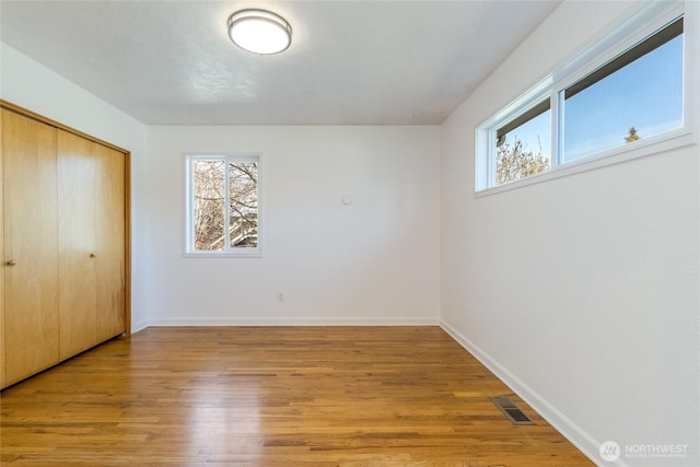 unfurnished bedroom with light wood-type flooring, visible vents, multiple windows, and a closet