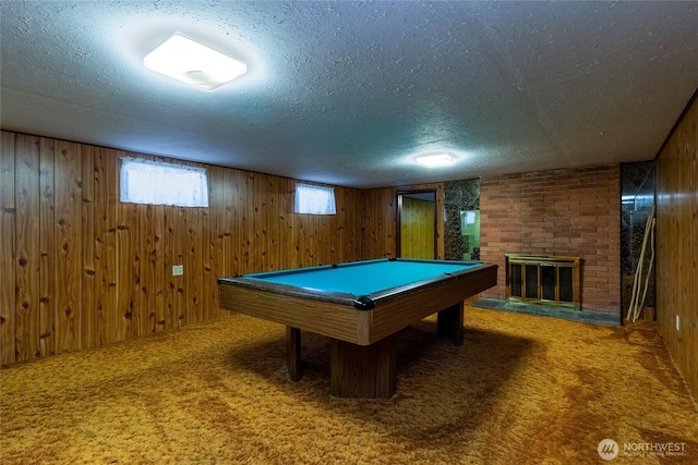 rec room featuring wooden walls, a textured ceiling, a brick fireplace, and carpet flooring