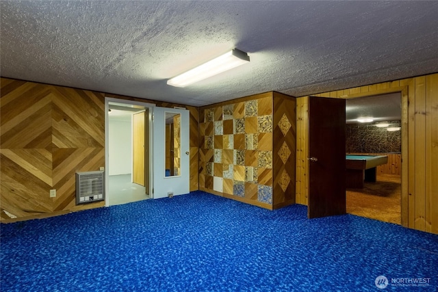 carpeted empty room with heating unit, a textured ceiling, wood walls, and billiards