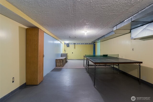 rec room with a textured ceiling, baseboards, and finished concrete floors