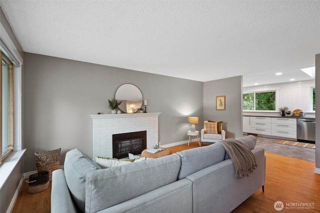 living area featuring a fireplace, recessed lighting, light wood-style flooring, a textured ceiling, and baseboards