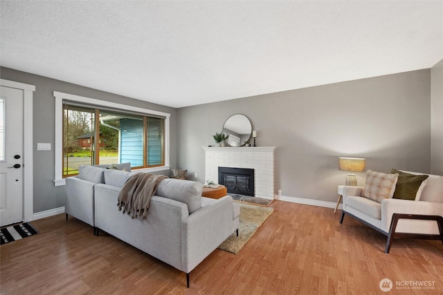 living room featuring light wood-style floors, a brick fireplace, a textured ceiling, and baseboards