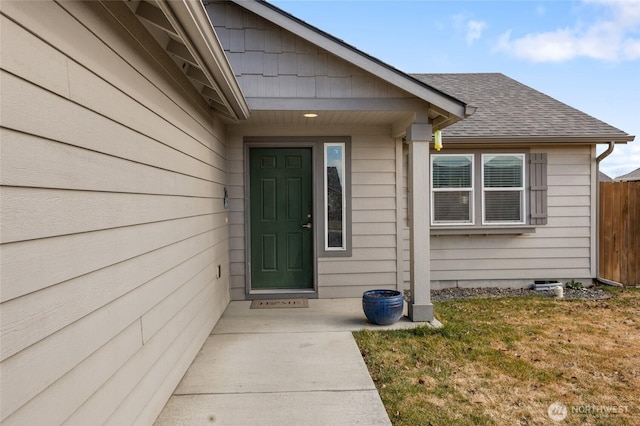 entrance to property with roof with shingles, fence, and a lawn