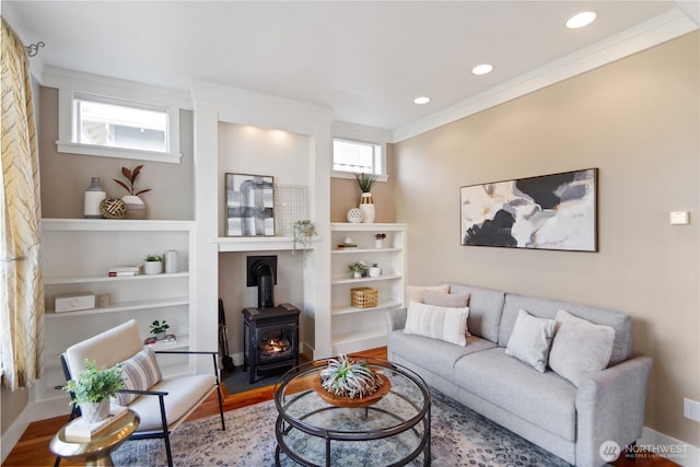 living room with built in shelves, wood finished floors, a wood stove, recessed lighting, and crown molding