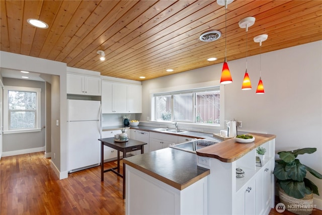 kitchen with visible vents, a sink, freestanding refrigerator, stovetop, and white cabinets