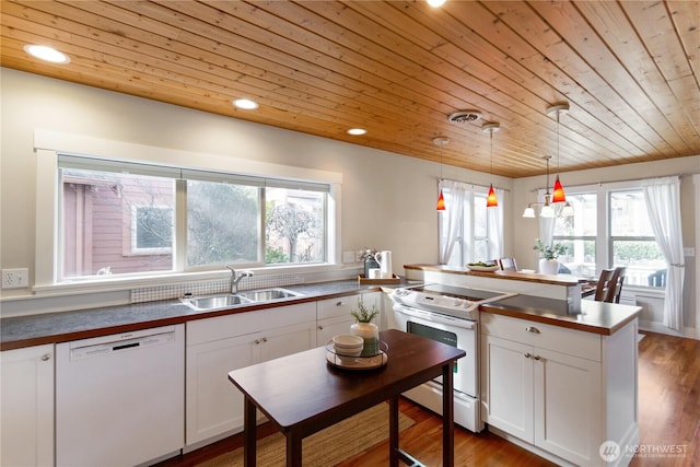 kitchen with white appliances, a peninsula, a sink, white cabinetry, and dark countertops