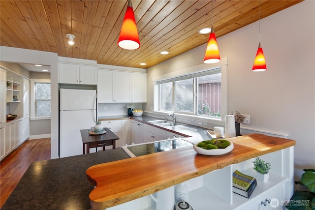 kitchen with butcher block counters, wood ceiling, freestanding refrigerator, and a sink