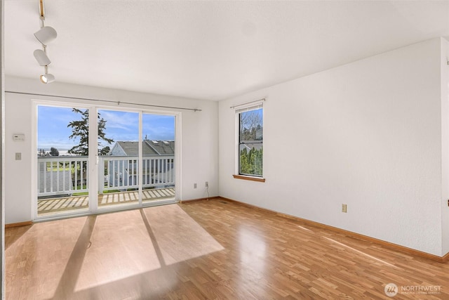 spare room featuring track lighting, baseboards, and wood finished floors