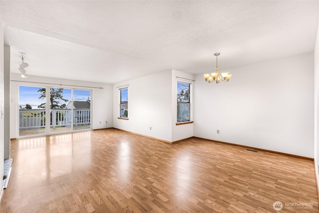 unfurnished room featuring a textured ceiling, baseboards, an inviting chandelier, and wood finished floors