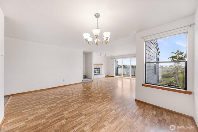 unfurnished living room with a chandelier, baseboards, light wood-style floors, and a glass covered fireplace