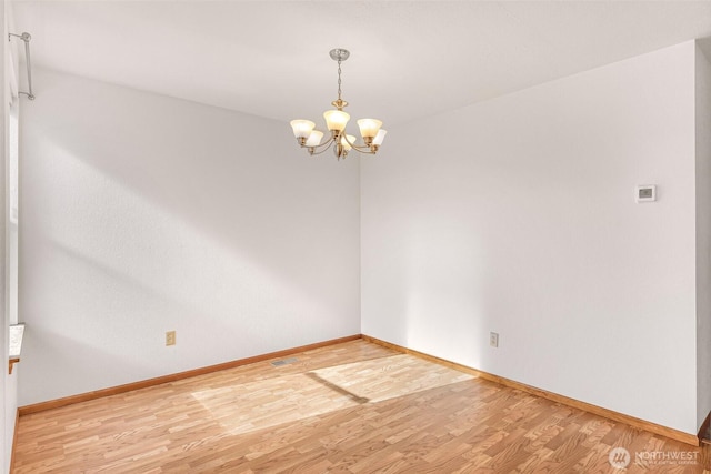 unfurnished room featuring a notable chandelier, baseboards, and light wood-type flooring