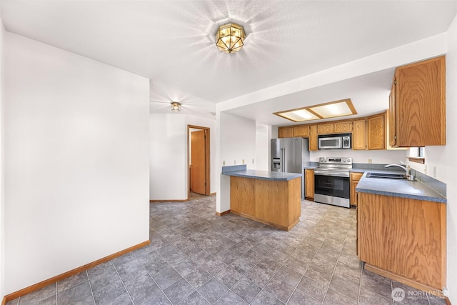 kitchen with a peninsula, a sink, stainless steel appliances, dark countertops, and brown cabinets