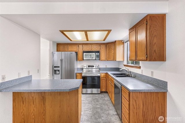 kitchen featuring a peninsula, a sink, stainless steel appliances, dark countertops, and brown cabinets