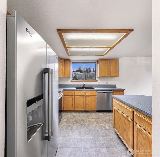 kitchen featuring brown cabinetry, light tile patterned flooring, a sink, stainless steel appliances, and dark countertops