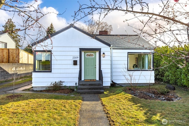 bungalow-style house with entry steps, a chimney, fence, and a front yard