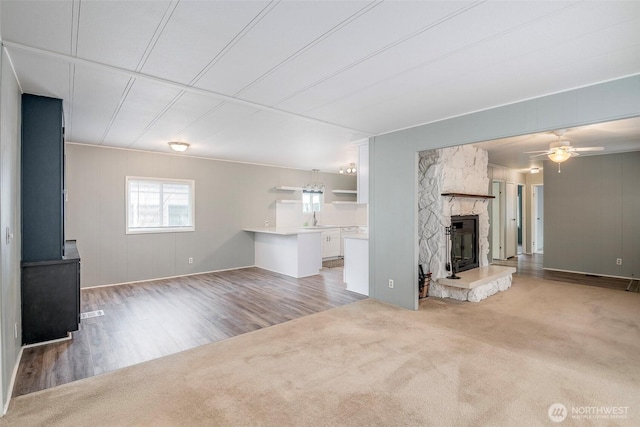 unfurnished living room featuring a stone fireplace, light colored carpet, and a ceiling fan