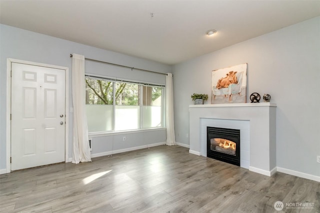 unfurnished living room with baseboards, wood finished floors, and a tile fireplace