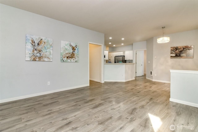 unfurnished living room with a notable chandelier, recessed lighting, light wood-type flooring, and baseboards