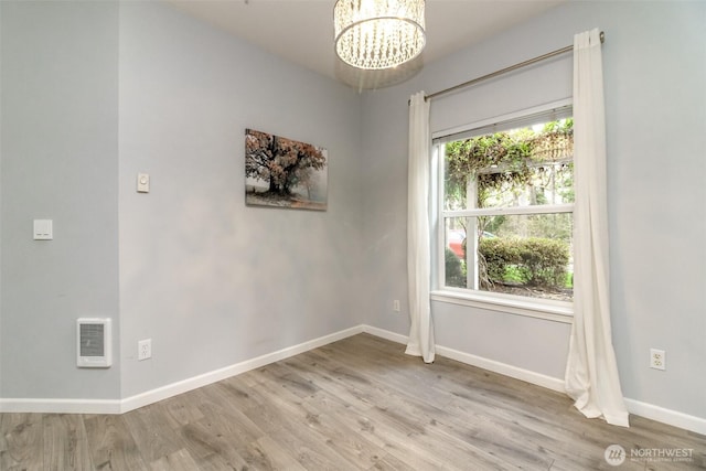 empty room featuring an inviting chandelier, wood finished floors, and baseboards