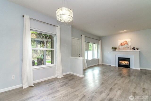 unfurnished living room featuring a chandelier, a glass covered fireplace, baseboards, and wood finished floors