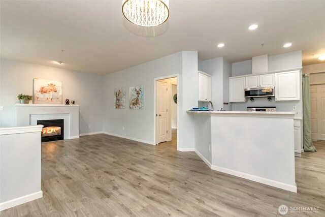 kitchen featuring white cabinetry, light wood-style flooring, recessed lighting, a glass covered fireplace, and stainless steel microwave