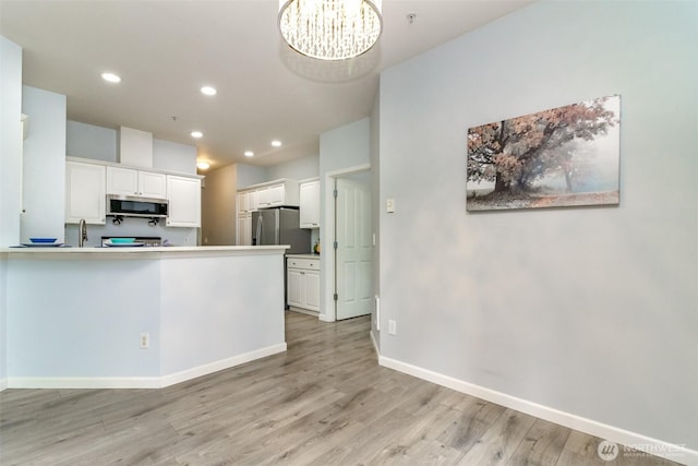 kitchen featuring baseboards, appliances with stainless steel finishes, a peninsula, light wood-style floors, and white cabinetry