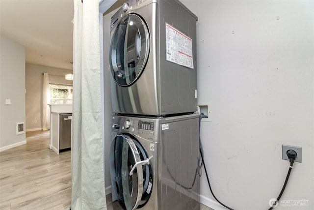 clothes washing area with visible vents, light wood finished floors, stacked washer / drying machine, baseboards, and laundry area