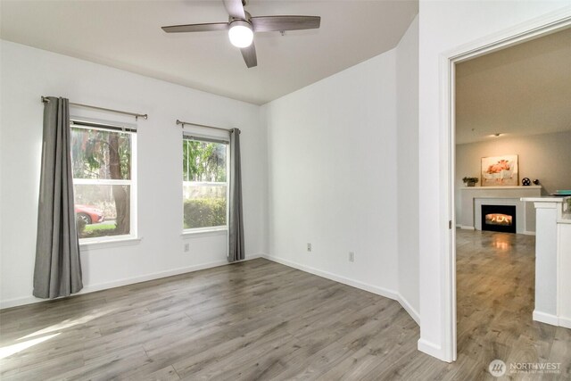 spare room with ceiling fan, wood finished floors, baseboards, and a lit fireplace