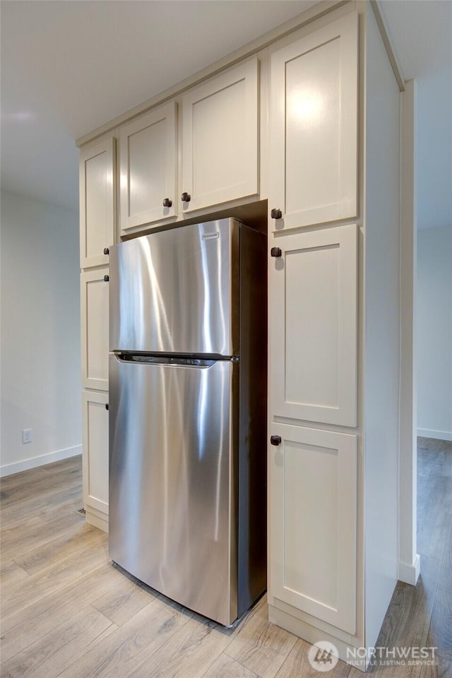 kitchen with light wood-style flooring, baseboards, white cabinets, and freestanding refrigerator