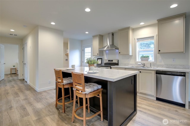 kitchen with visible vents, appliances with stainless steel finishes, light countertops, wall chimney range hood, and a sink