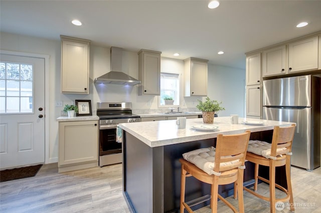 kitchen featuring stainless steel appliances, a kitchen island, a kitchen breakfast bar, light countertops, and wall chimney exhaust hood